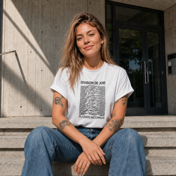 Femme portant le t-shirt blanc Division de Joie devant une entrée d’immeuble brutaliste